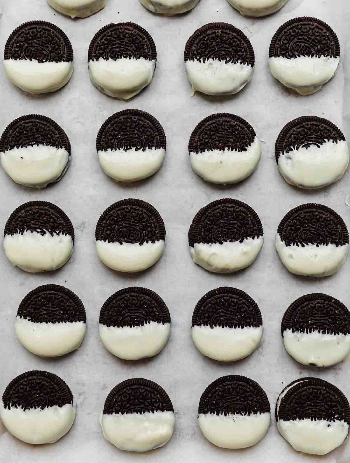 Half dipped white chocolate Oreos on a parchment paper lined baking sheet.