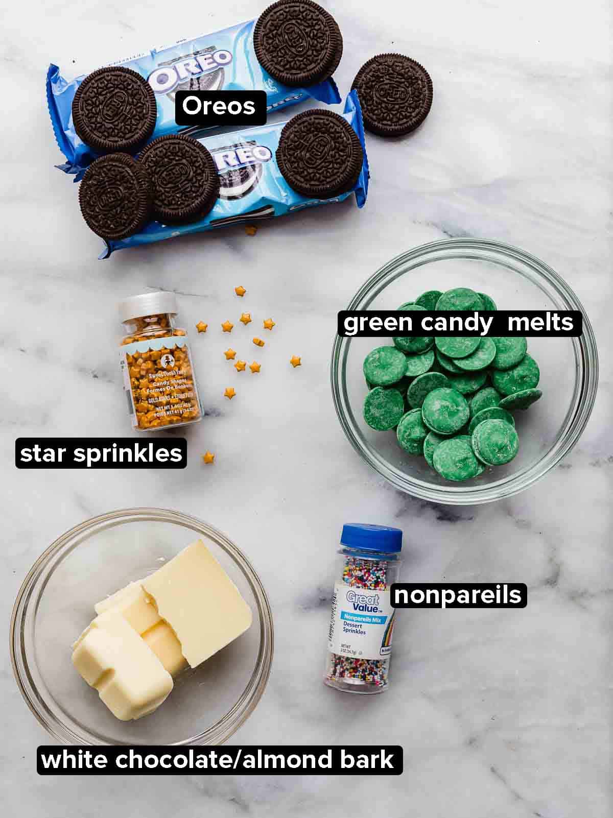 Christmas Tree Oreos ingredients on a white marble background: Oreos, green candy melts, white chocolate, nonpareil sprinkles, and star sprinkles.