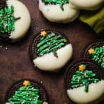 Christmas Tree Oreos on a brown background, an Oreo half dipped in white chocolate with a green Christmas tree piped on the Oreos and topped with nonpareil sprinkles.