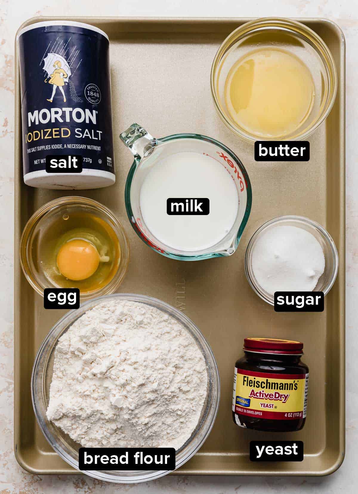 Pecan Sticky Buns ingredients on a bronze baking sheet: salt, flour, milk, butter, egg, yeast, and sugar.