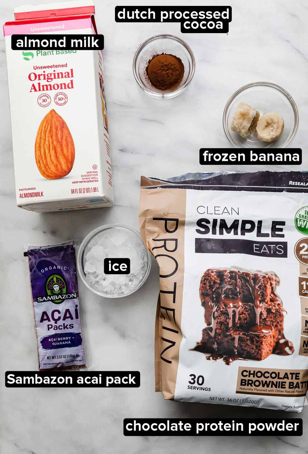Chocolate Acai Bowl ingredients on a white background: chocolate protein powder, açaí packet, almond milk, ice, frozen banana, cocoa powder.