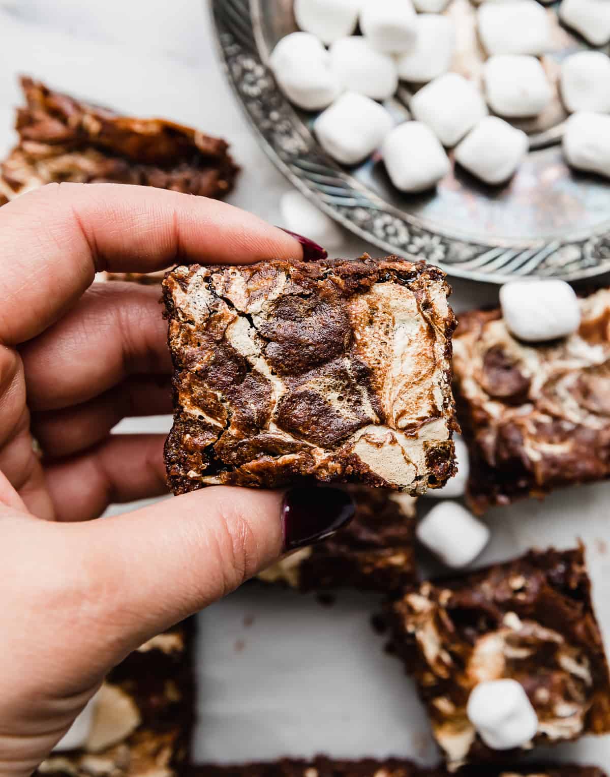 A hand holding a square of Marshmallow Brownies, with marshmallow creme swirled into the top.