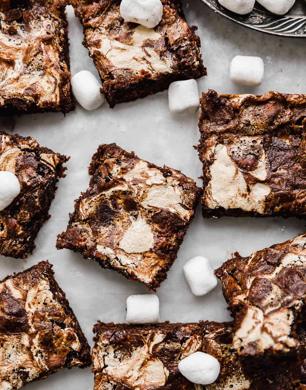 Overhead photo of Marshmallow Brownies cut into squares on a white parchment paper with mini marshmallows scattered around.