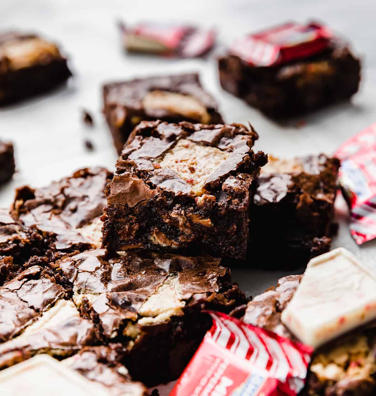 Squares of Peppermint Bark Brownies made from Ghirardelli brownie mix, on a white background with red peppermint bark packaging surrounding the brownies.