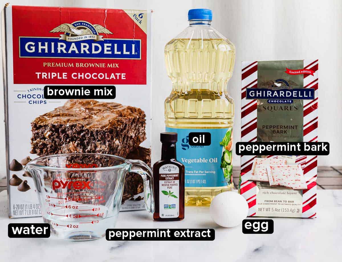 Peppermint Bark Brownies ingredients against a white background, brownie mix, oil, Ghirardelli peppermint bark package, egg, water, and peppermint extract.