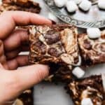 A hand holding a Marshmallow Brownie that has marshmallow cream/fluff that was swirled into the top of the brownie before baking.