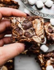A hand holding a Marshmallow Brownie that has marshmallow cream/fluff that was swirled into the top of the brownie before baking.