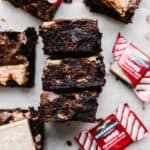 Peppermint Bark Brownies on white background with a few Ghirardelli red packaged peppermint barks near the brownies.