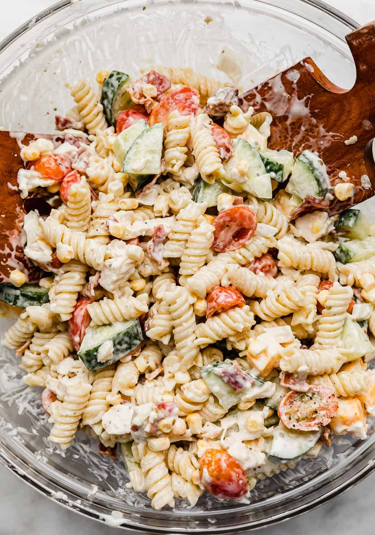 Close up photo of Chicken Bacon Ranch Pasta Salad in a glass bowl on a white background. 