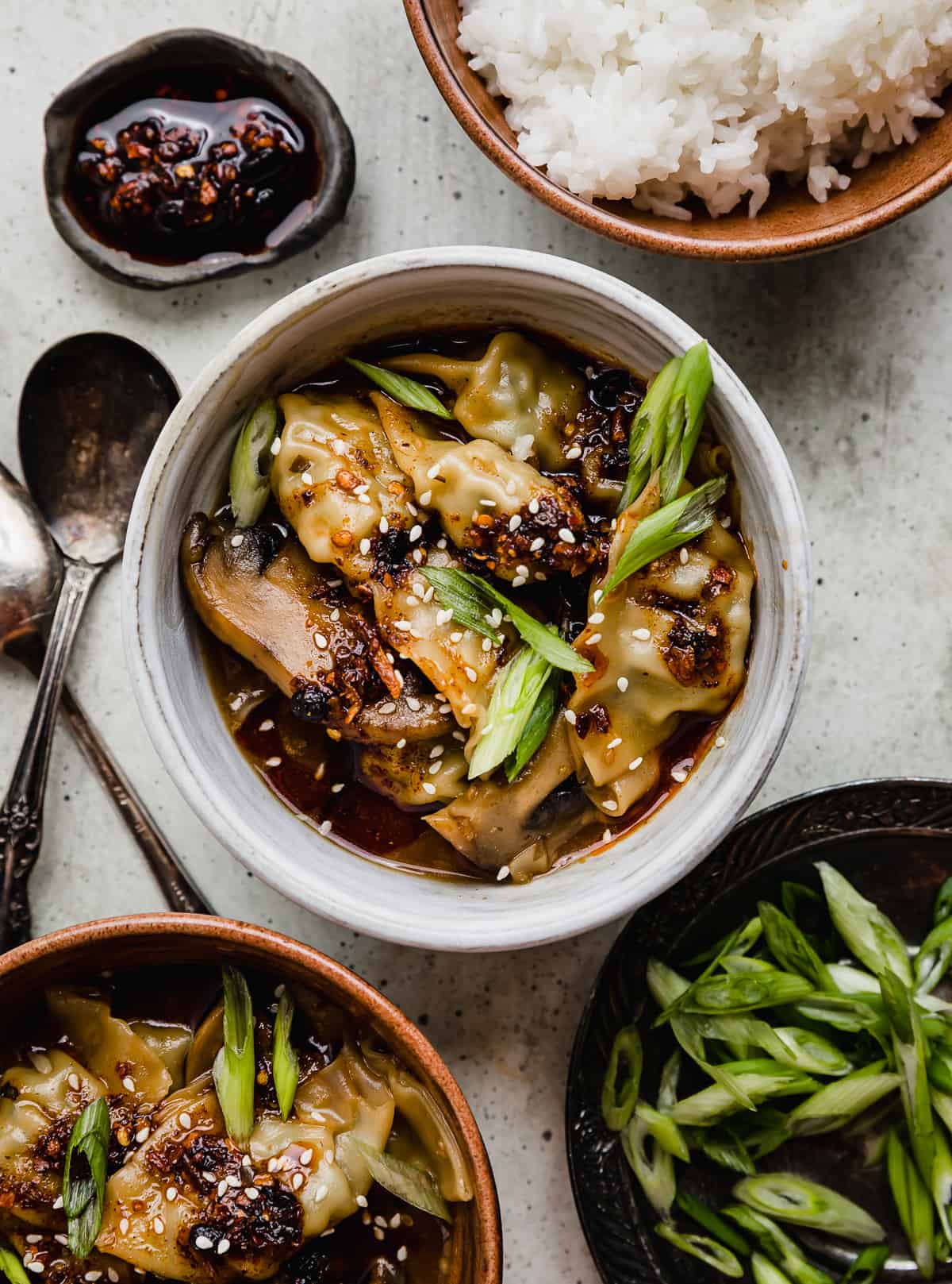 Spicy Chicken Wontons topped with sliced scallions in a white bowl on a light gray background.