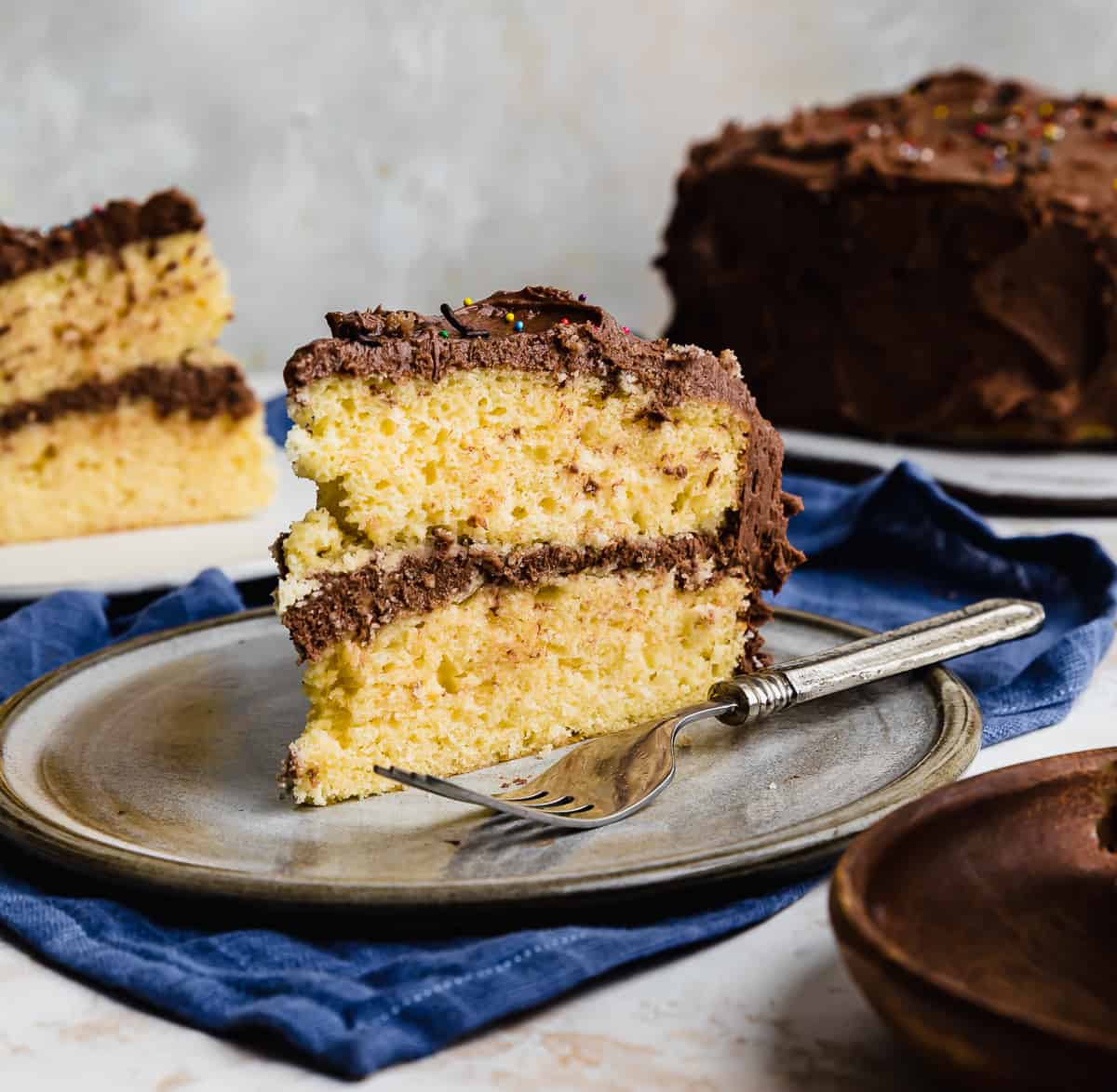 A slice of two layer yellow cake recipe with chocolate frosting on a gray plate.