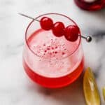 Pink Lady Mocktail in a small glass with three maraschino cherries on a cocktail stick.