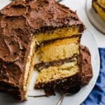 A slice of yellow cake topped with chocolate frosting on a white cake plate.
