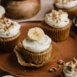 Banana Cupcakes topped with cream cheese frosting and a banana slice, on a brown plate.
