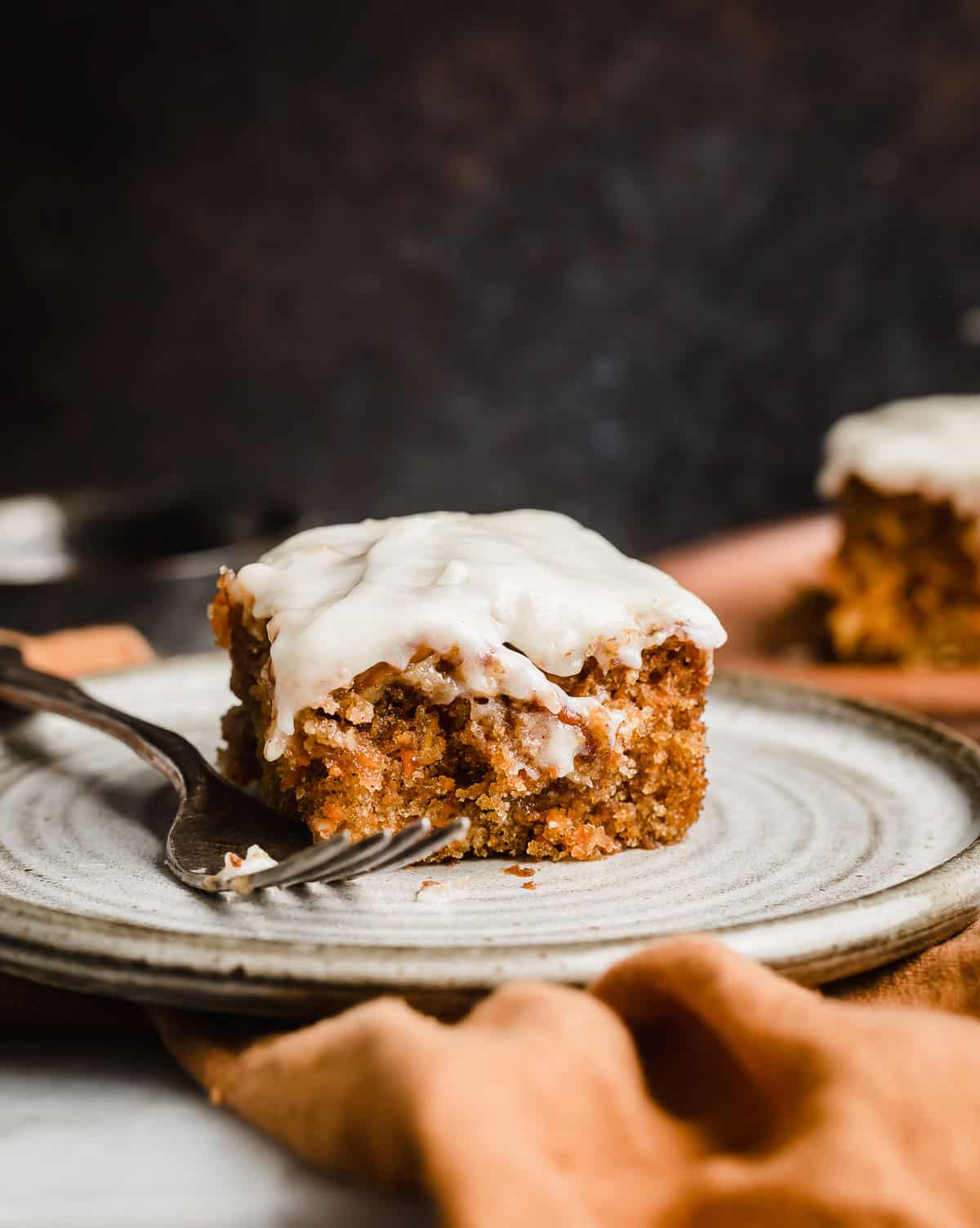 A square of Carrot Coffee Cake topped with a pecan streusel and cream cheese glaze/frosting on a white plate.