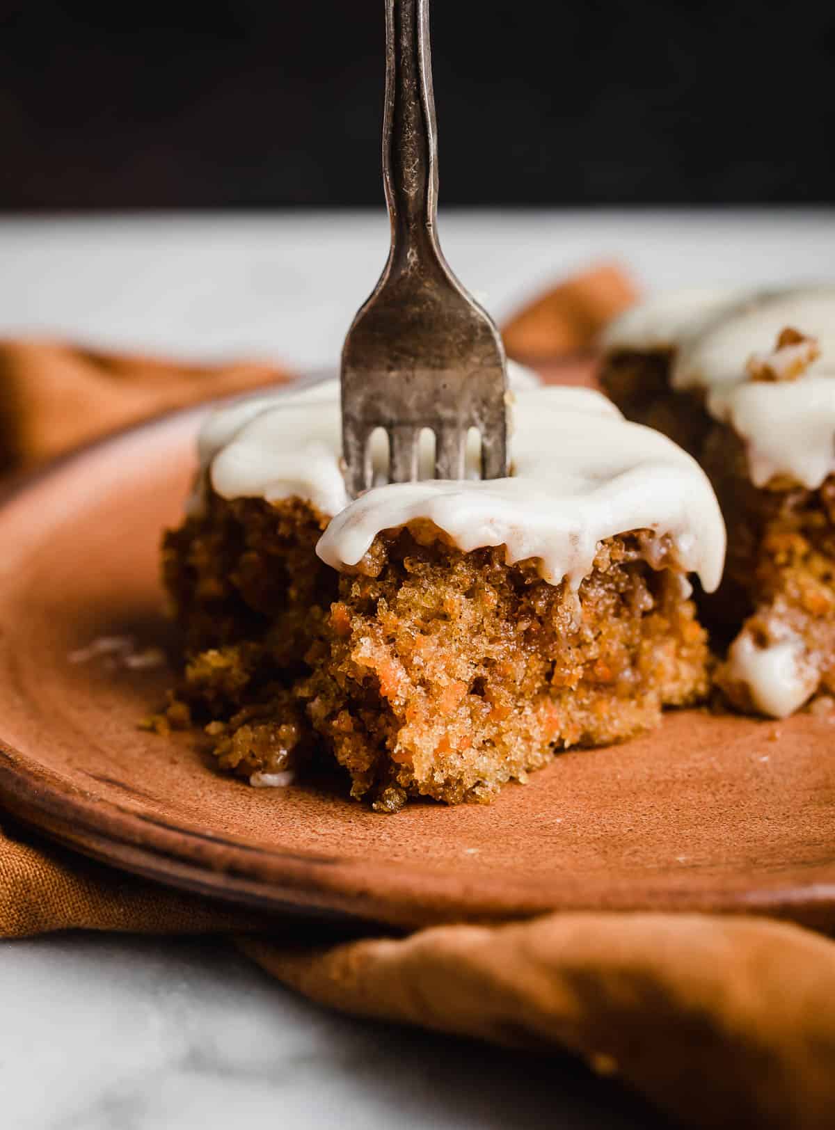A fork cutting into a slice of moist carrot cake coffee cake on a brown plate.
