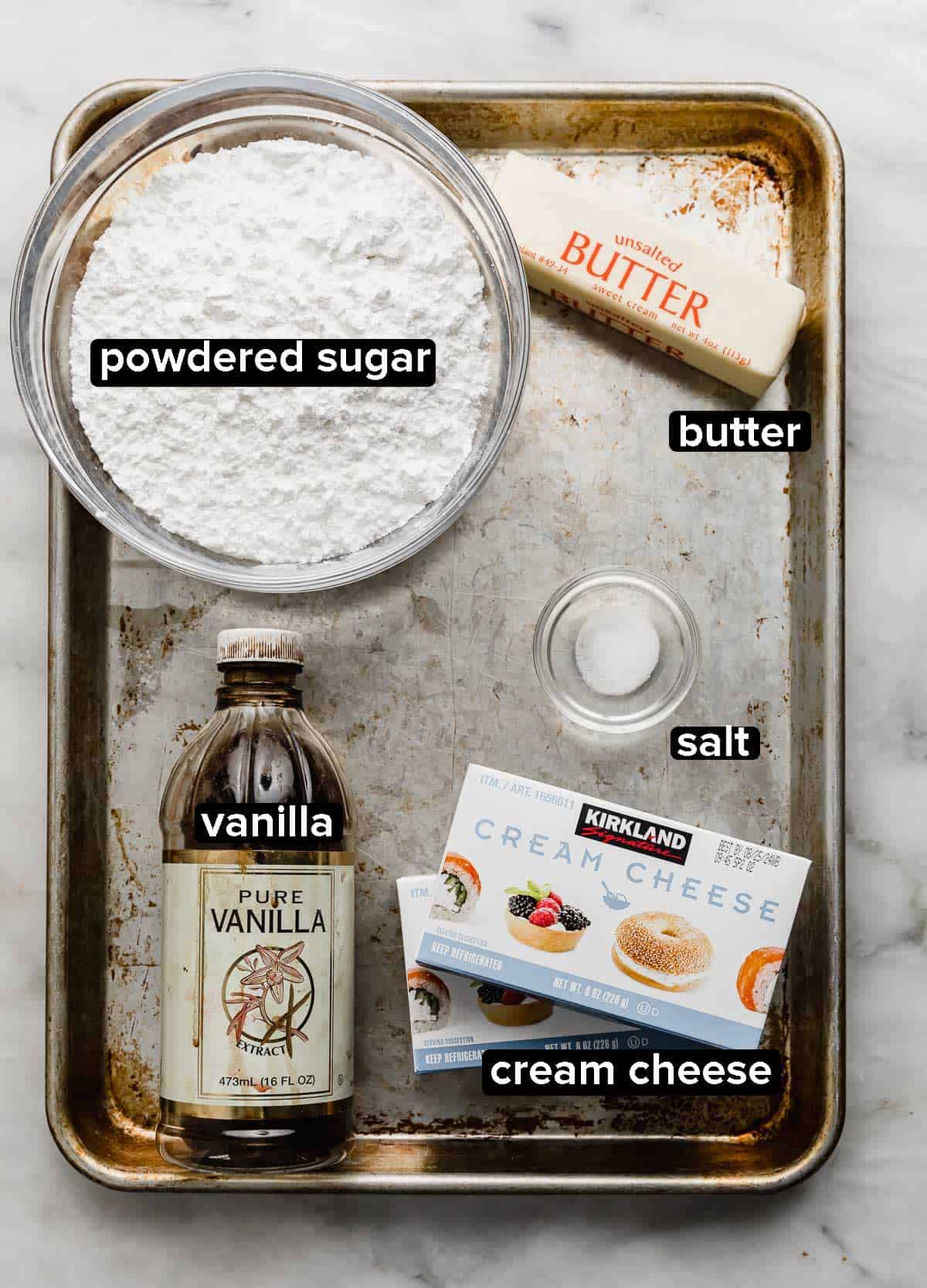 Ingredients used to make Small Batch Cream Cheese Frosting recipe on a baking sheet: cream cheese, butter, powdered sugar, vanilla, and salt.