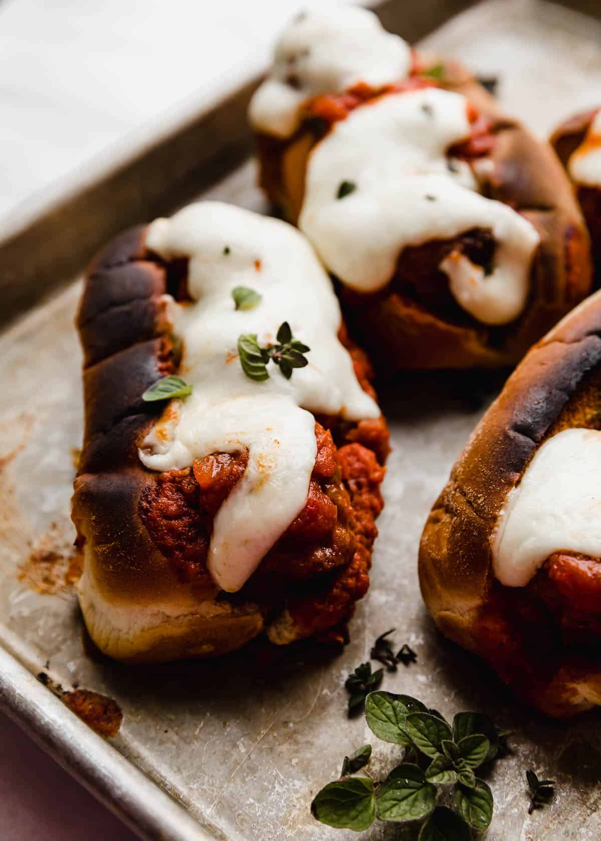 Italian Meatball Subs topped with melty mozzarella cheese and a garnish of fresh oregano on a baking sheet.