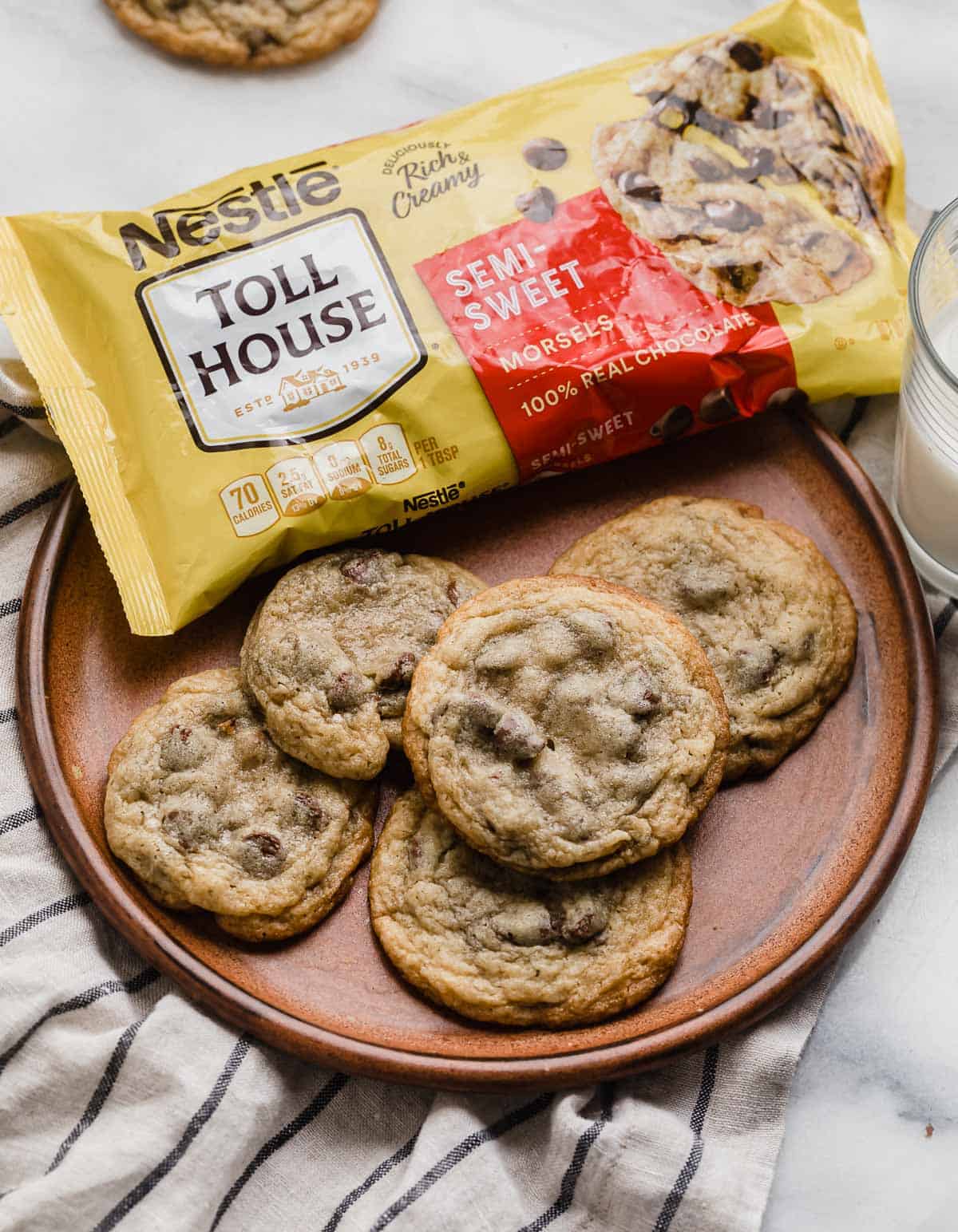 Nestle Toll House Chocolate Chip Cookies on a brown plate with a bag of Nestle chocolate chips in the background.