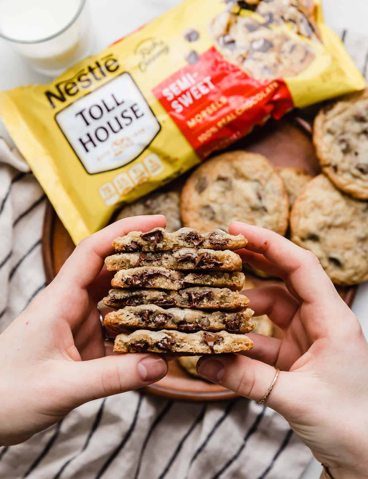 A hand holding a stack of chocolate chip nestle toll house cookies that have been cut in half.