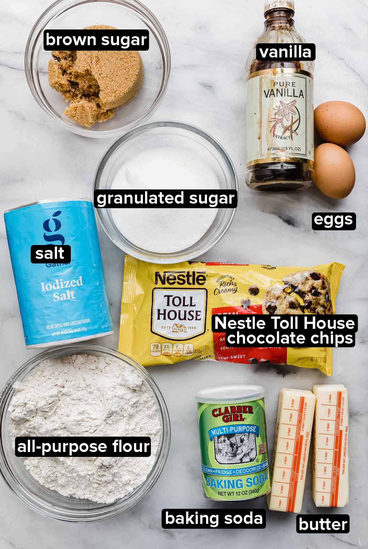 Nestle Toll House Chocolate Chip Cookie recipe ingredients on a white background: salt, flour, butter, baking soda, semi-sweet chocolate chips, sugar, and brown sugar, and eggs.