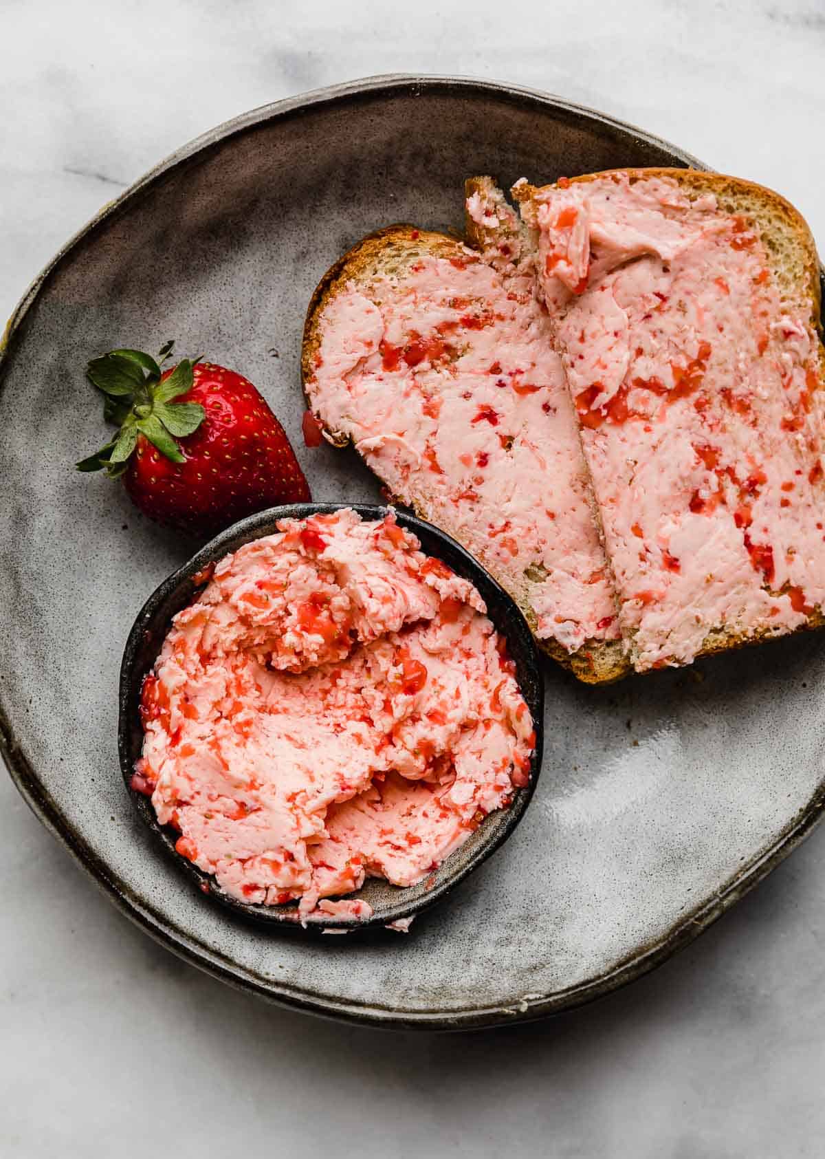 Strawberry Butter smeared on two slices of bread on a gray plate.