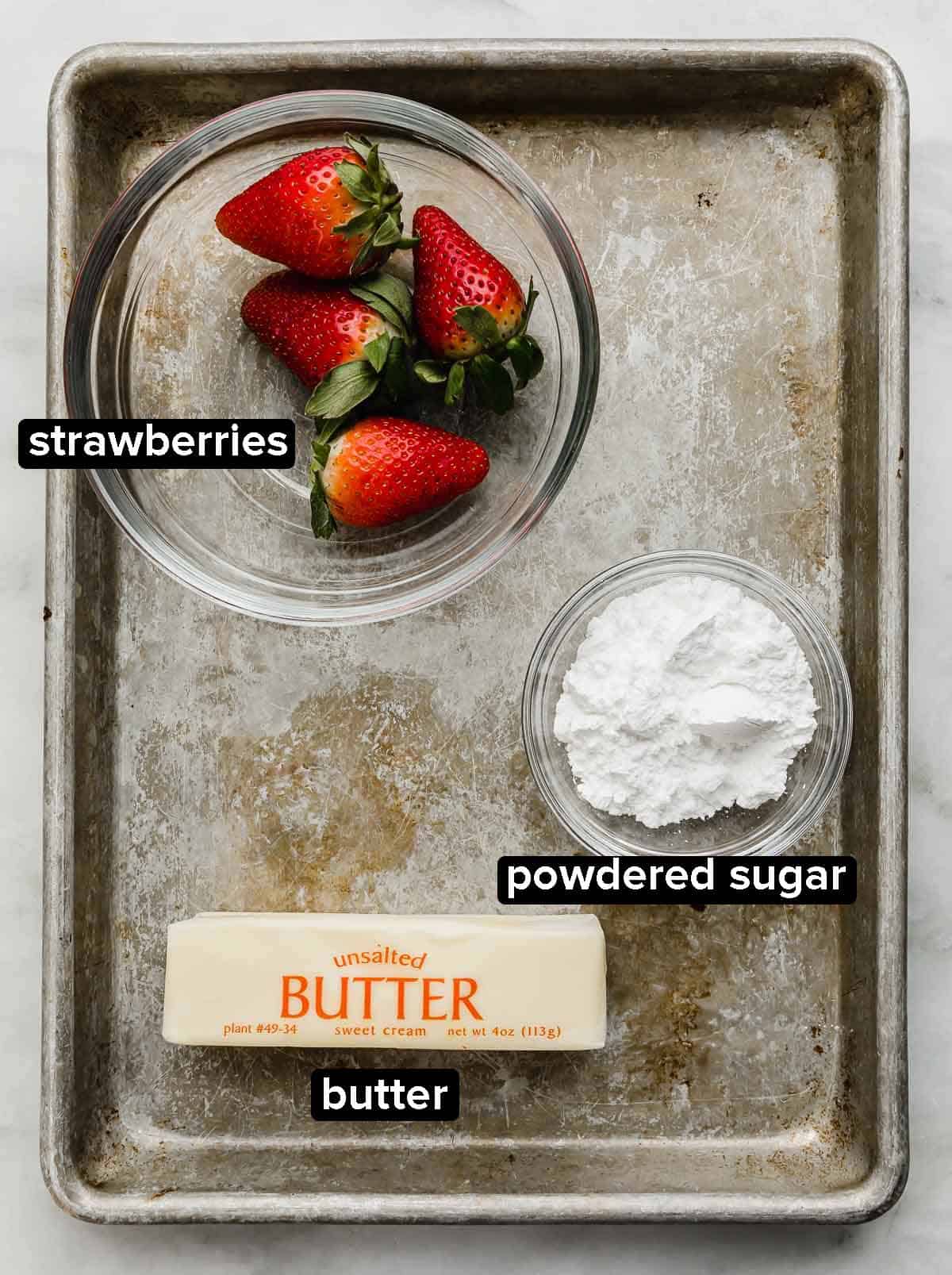 Strawberry Butter ingredients portioned into glass bowls on a metal baking sheet: fresh strawberries, powdered sugar, and a cube of unsalted butter.