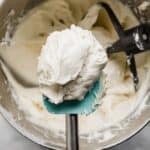 Small Batch Cream Cheese Frosting recipe on a turquoise rubber spatula over a bowl of cream cheese frosting.