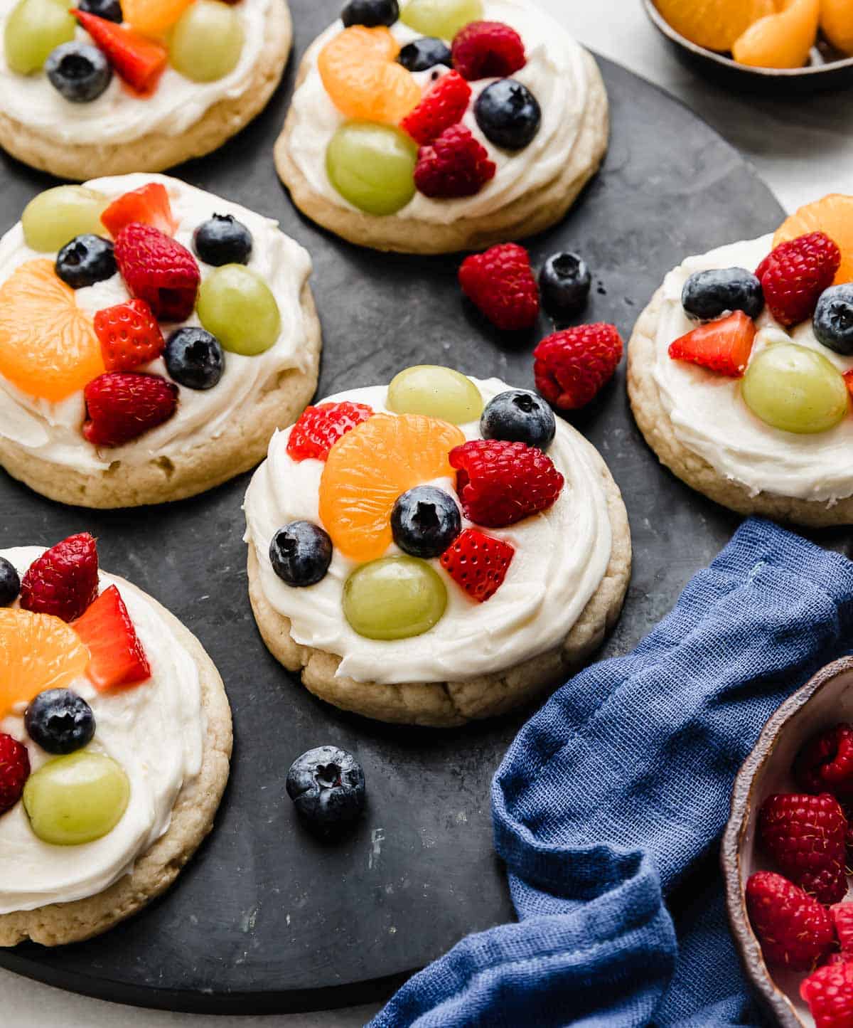 Fruit Pizza Cookies topped with a cream cheese frosting and topped with raspberries, blueberries, grapes, and mandarin oranges.