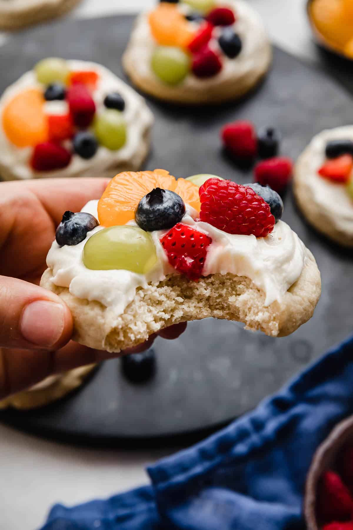 A hand holding the best Fruit Pizza Cookie topped with a cream cheese frosting and fresh fruit.