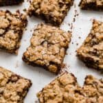 The best oatmeal cookie bars with chocolate chips, cut into squares on a white background with crumbs surrounding each brown butter oatmeal bar.