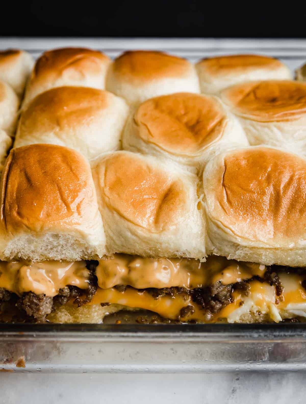 Baked Hawaiian Roll Breakfast Sliders in a glass baking pan showing the layers of scrambled eggs, cheese, and sausage.