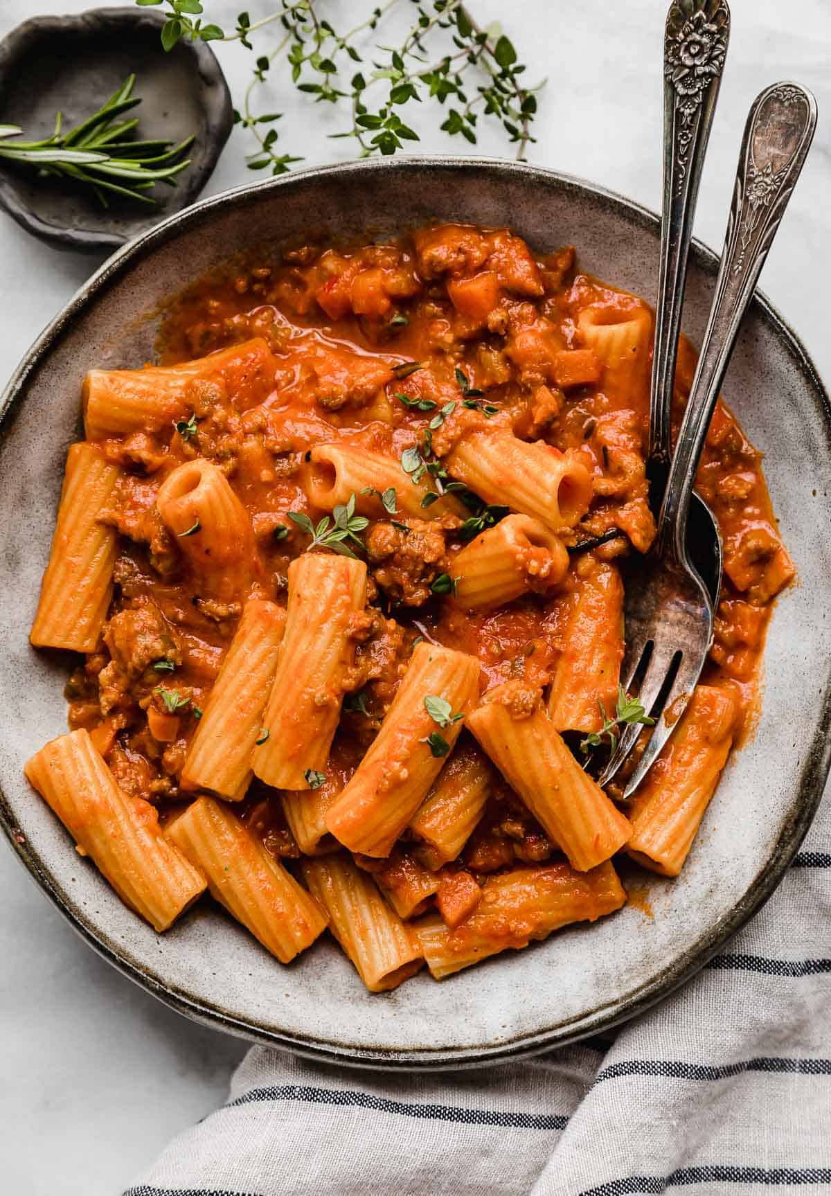 A gray pasta bowl filled with creamy Sausage Ragu with fresh herbs on a white surface.