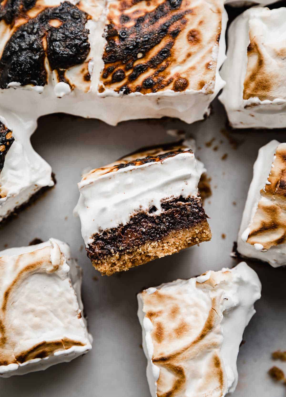 S'mores Brownies cut into squares, with one S'more brownie on its side showcasing the graham cracker crust, fudgy brownie, and homemade toasted marshmallow cream topping.