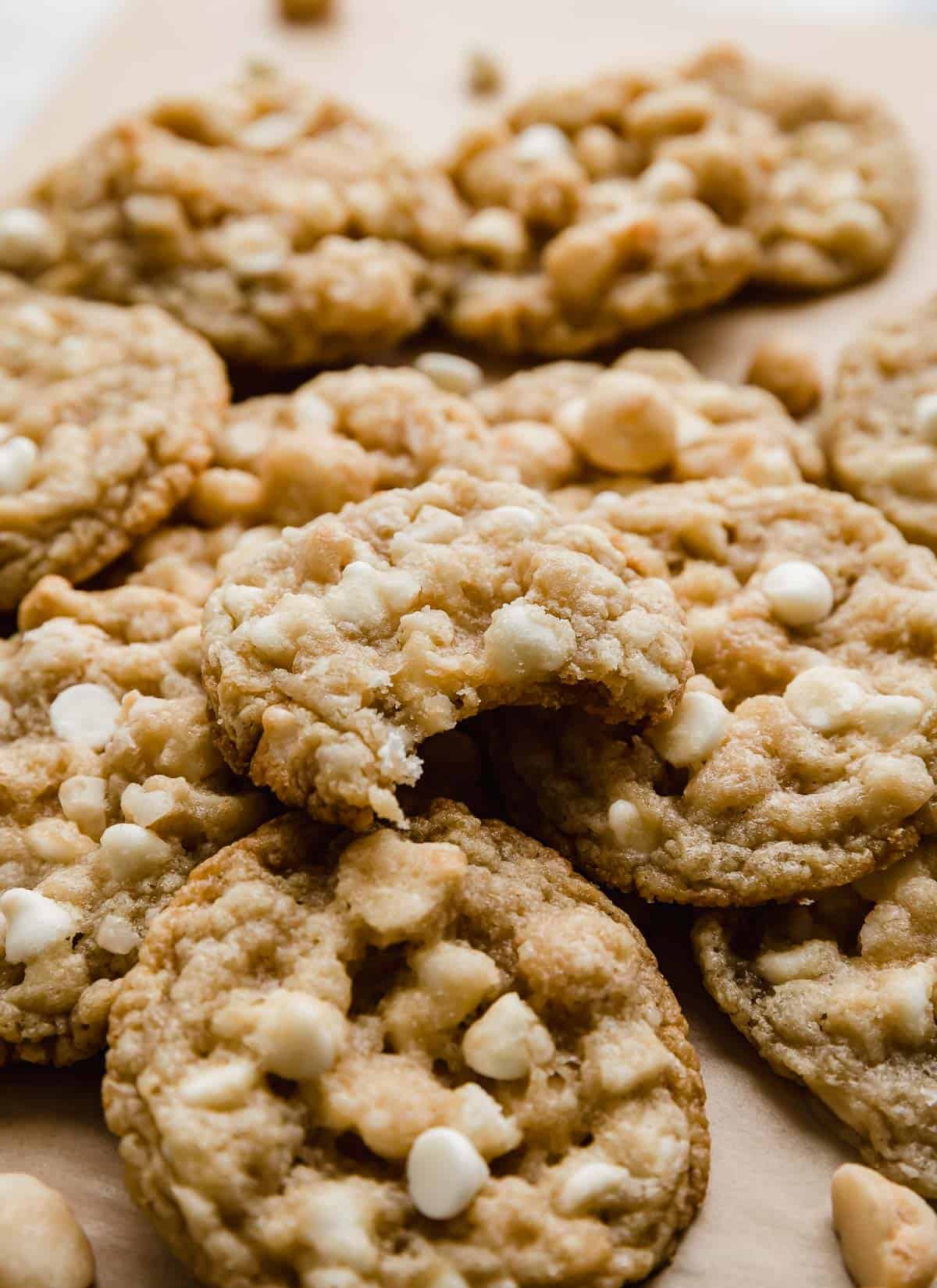 A White Chocolate Macadamia Nut Cookie with a bite taken out of it, stacked on a small pile of other macadamia nut white chocolate chip cookies.