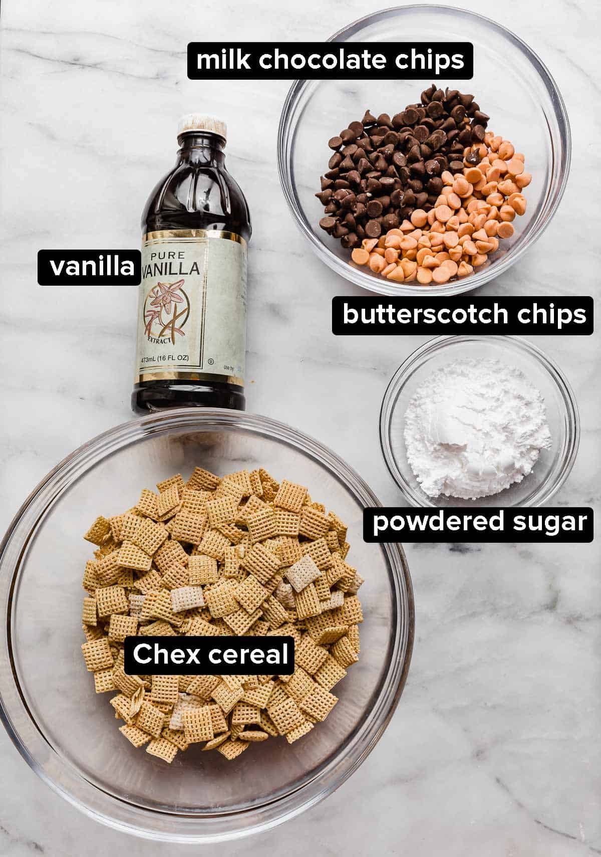 Butterscotch Puppy Chow ingredients on a white marble surface; Chex cereal, powdered sugar, milk chocolate chips, butterscotch chips, and vanilla.