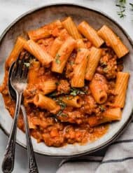 A fork and spoon in the bowl accompanied with delicious Sausage Ragu, on a white marble surface.