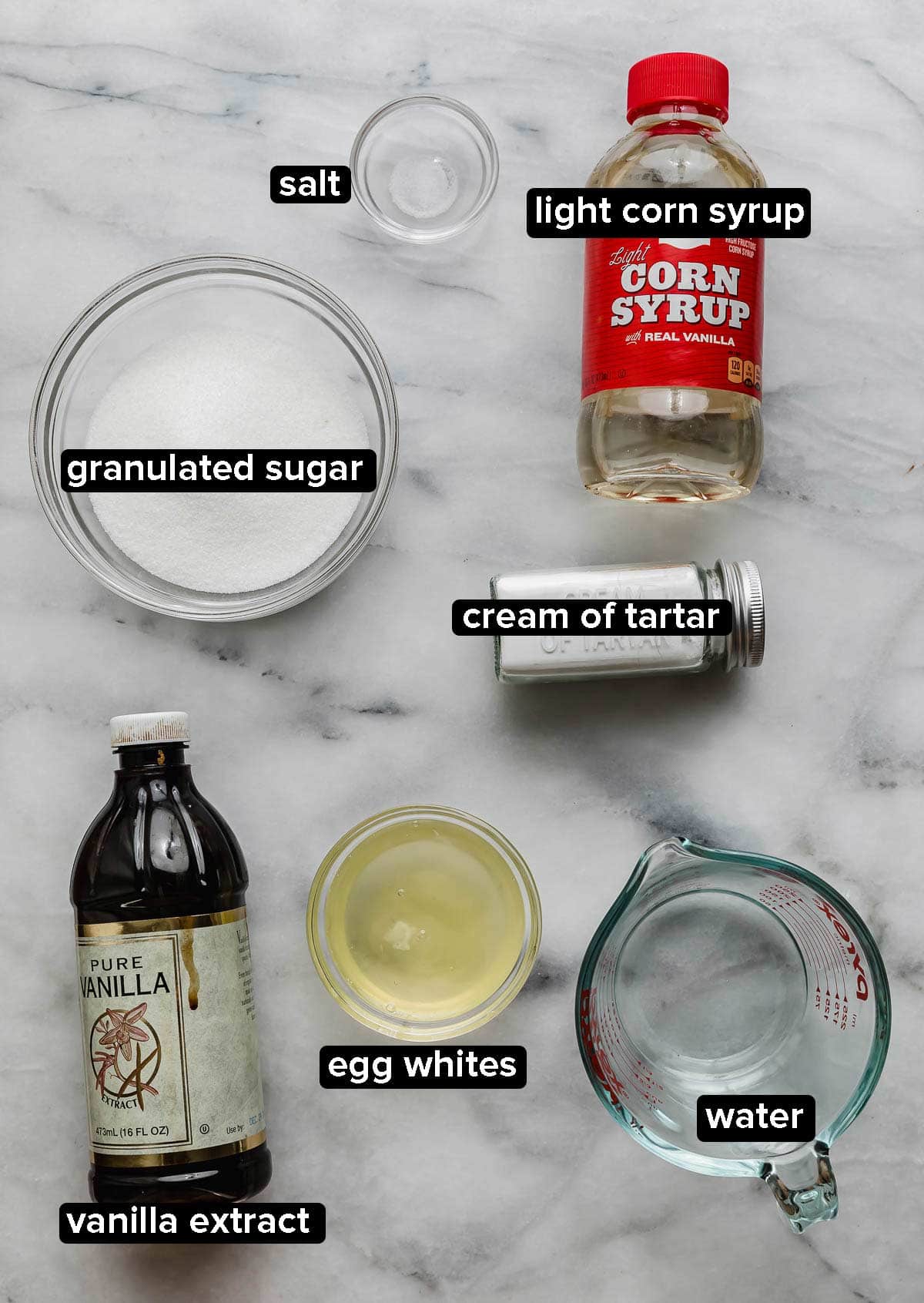 Homemade Marshmallow Cream ingredients on a white marble surface: egg whites, corn syrup, vanilla, water, sugar, and cream of tartar.