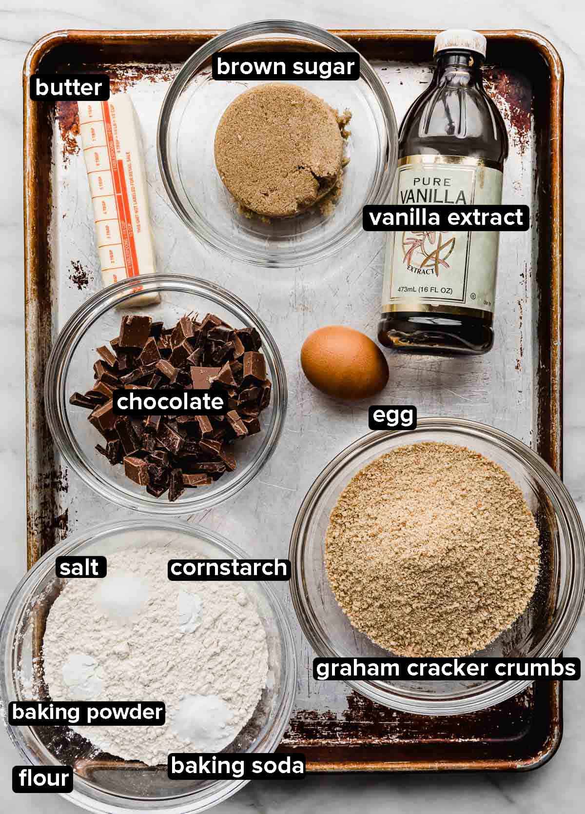 S'mores Cookie ingredients on a baking sheet: sugar, chocolate, graham cracker crumbs, butter, egg, and dry ingredients.