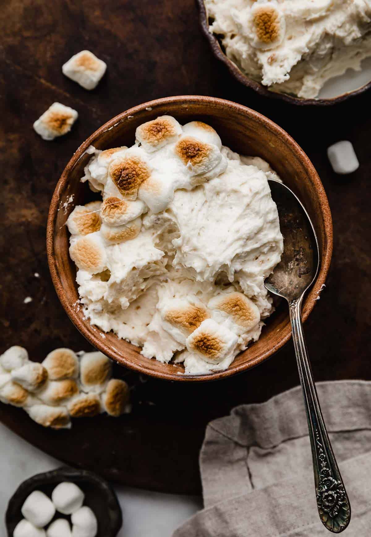 Toasted Marshmallow Frosting made with real toasted marshmallows, in a brown bowl on a dark brown surface.