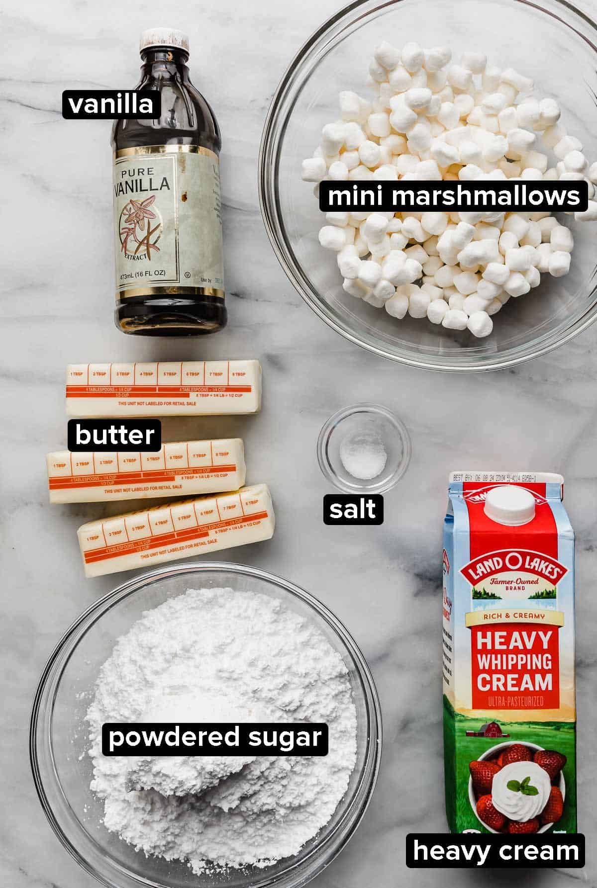 Toasted Marshmallow Frosting ingredients on a white surface: heavy cream, mini marshmallows, powdered sugar, butter, and vanilla extract.