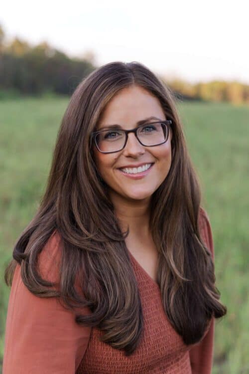 Whitney Wright wearing glasses with brown hair in a field of grass.