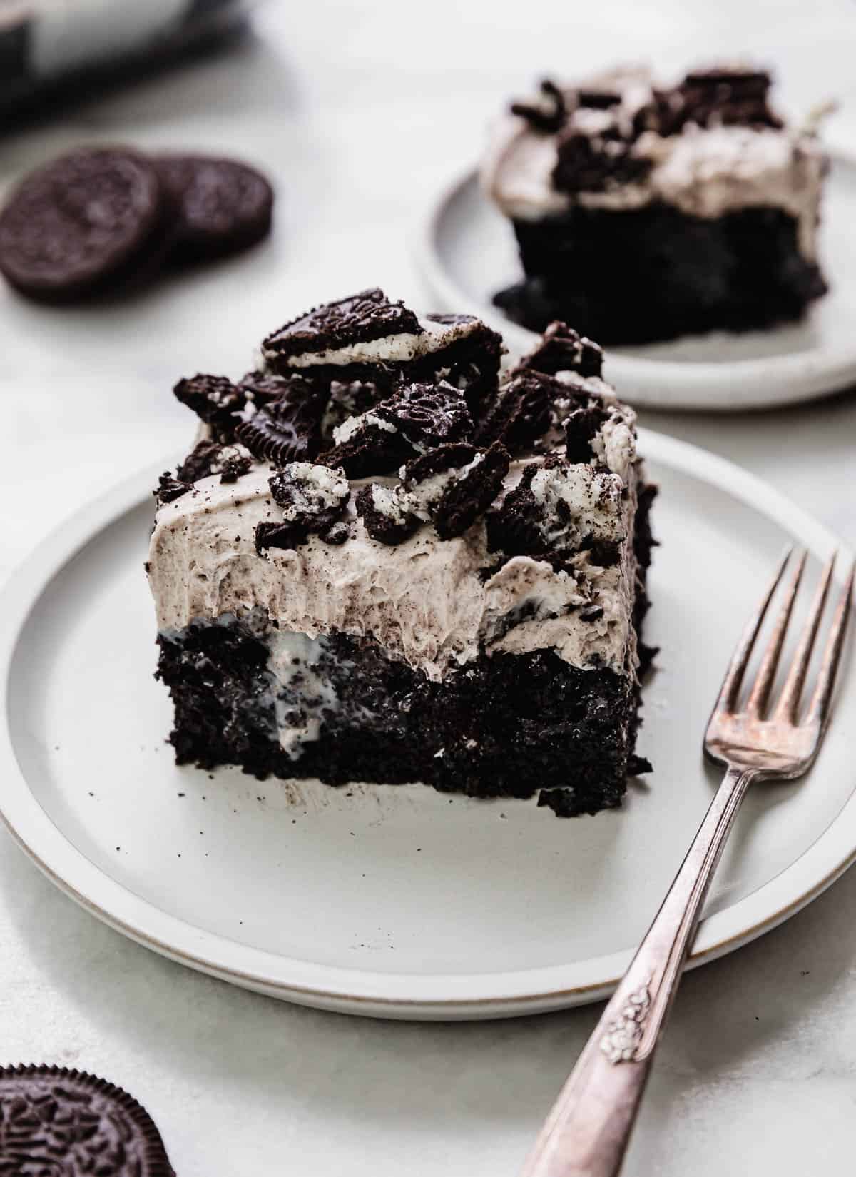 A square slice of Oreo Poke Cake drizzled with sweetened condensed milk and topped with a whipped Oreo cream pudding frosting.