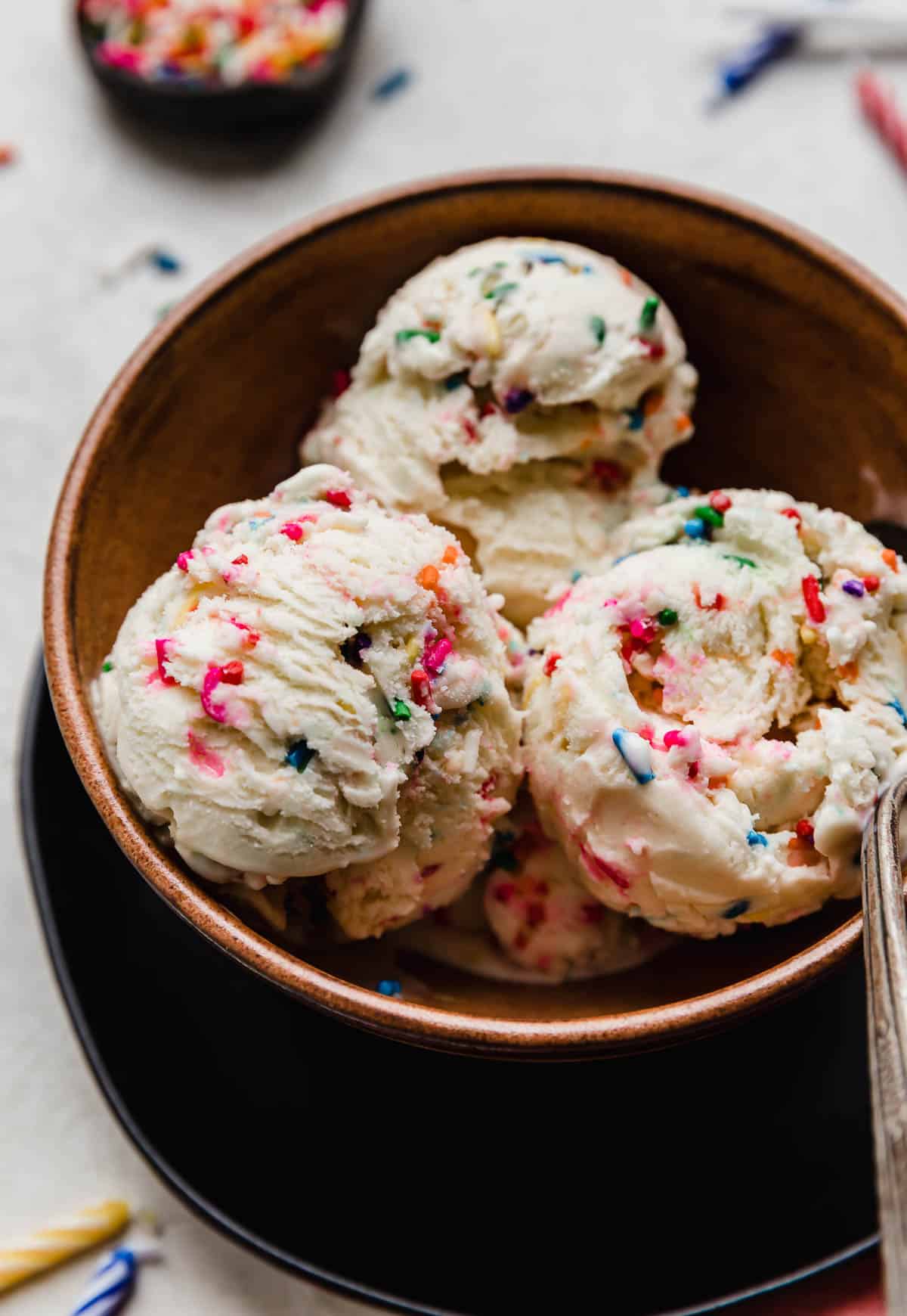 Three scoops of sprinkle loaded Birthday Cake Ice Cream in a brown bowl.