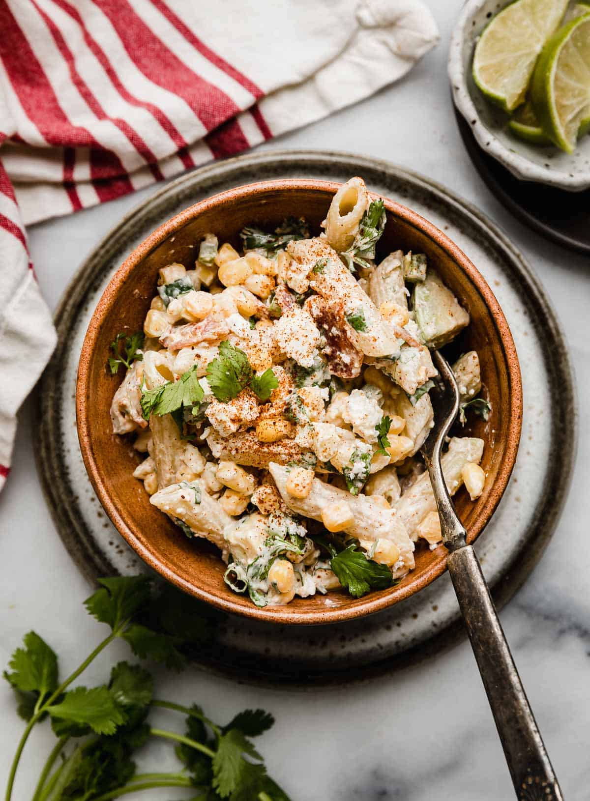 Mexican Street Corn Pasta Salad in a brown bowl on a white marble surface, garnished with cilantro. 