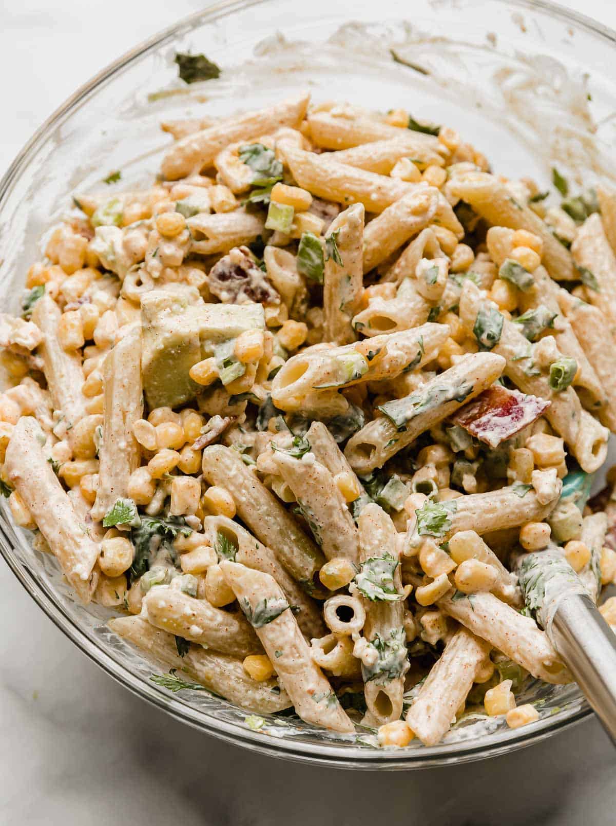 Mexican Street Corn Pasta Salad with corn, cilantro, and a mayo and sour cream dressing mixed into the bowl.