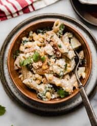 Creamy Mexican Street Corn Pasta Salad recipe in a brown bowl on a white marble surface.