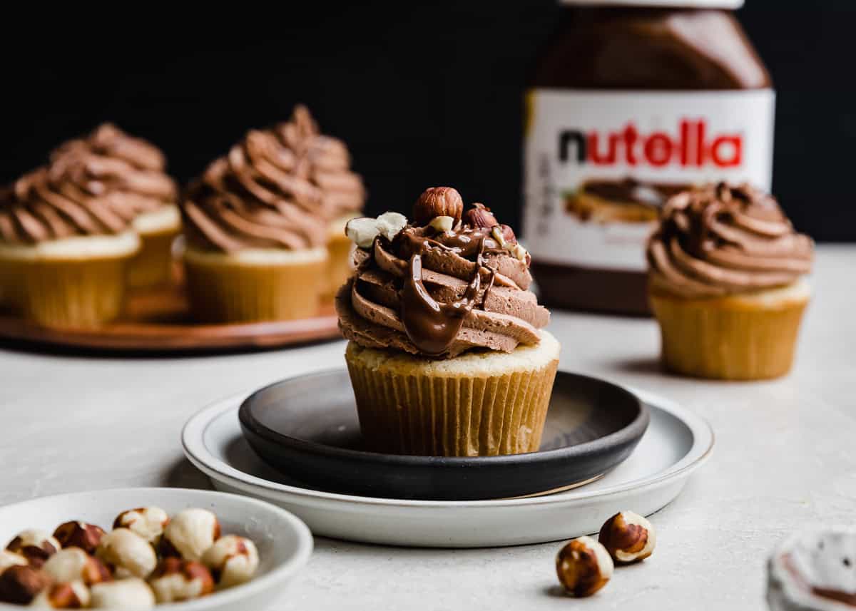 Vanilla cupcakes filled with Nutella and topped with a swirl of Nutella frosting against a black background. 