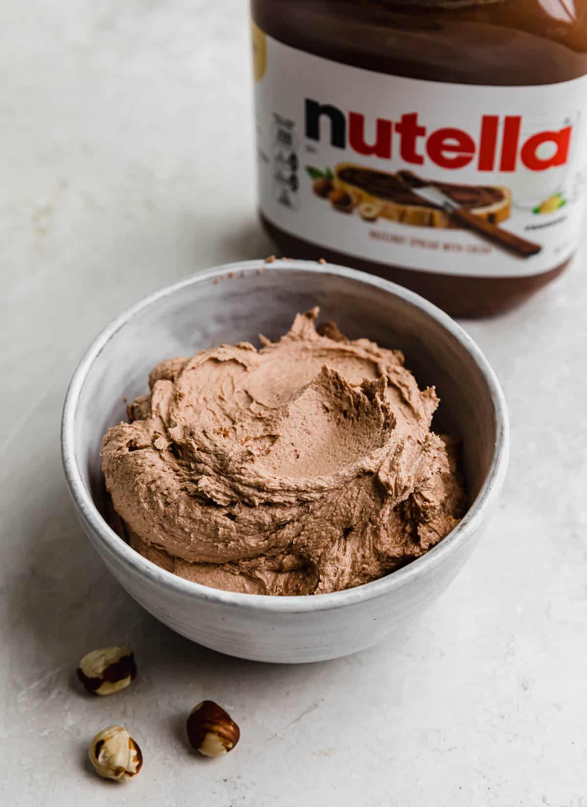 A white bowl filled with the best Nutella Frosting and a bottle of Nutella in the background.