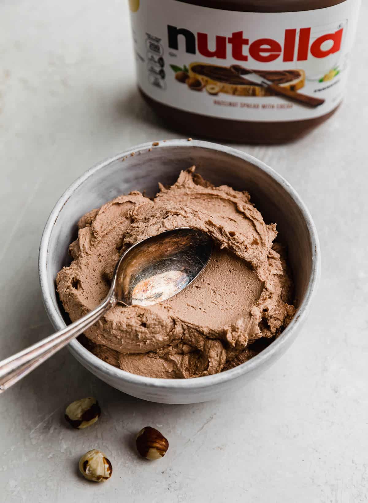 A spoon smearing Nutella Frosting in a white bowl.